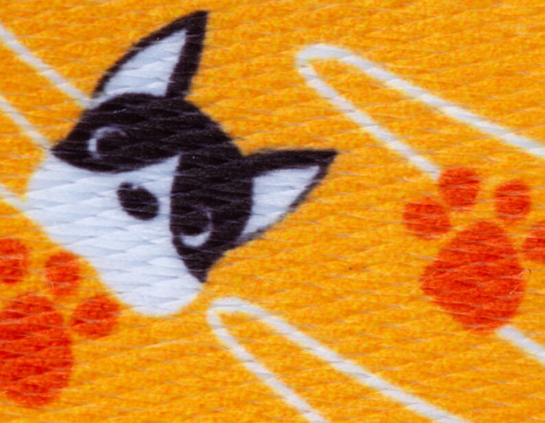May include: A yellow fabric with a white and black dog face and orange paw prints. The fabric has a textured surface.