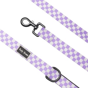 May include: A dog leash with a purple and white checkered pattern. The leash has a silver-colored metal clasp and a black metal D-ring. The brand name "Buly Bows" is printed on a black and white label.