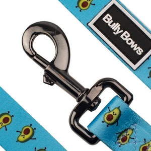 May include: A blue dog leash with a black metal clip and a repeating pattern of cartoon avocados. The leash has a black label that says "Bully Bows".