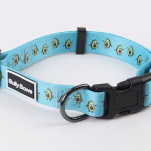 May include: A light blue dog collar with a repeating pattern of cartoon avocados. The collar has a black buckle and a black metal D-ring. The collar has a white label that says "Bully Bows".