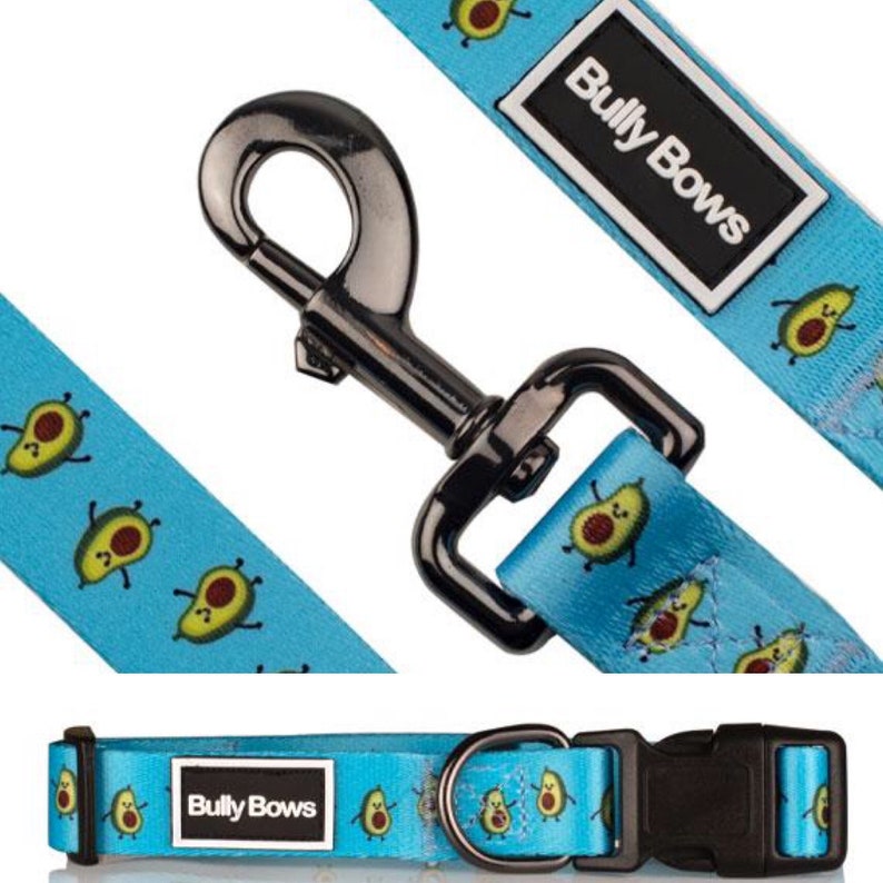 May include: A blue dog collar with a black buckle and a silver D-ring. The collar has a repeating pattern of avocado illustrations and the text "Bully Bows" in black.