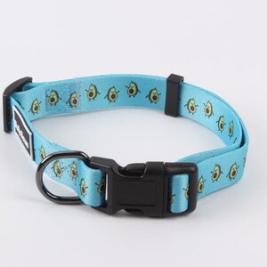 May include: A blue dog collar with a repeating pattern of cartoon avocados. The collar has a black buckle and a silver D-ring.