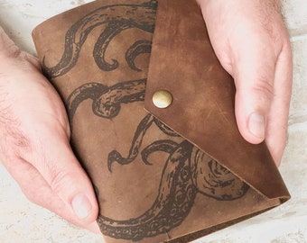 May include: A brown leather journal with a flap closure and a brass button. The journal features an embossed design of an octopus.