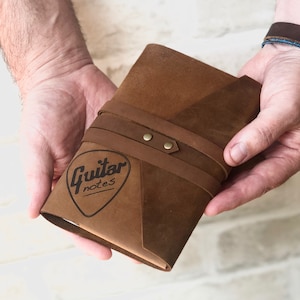 May include: A brown leather-bound journal with a guitar pick-shaped logo that says "Guitar notes".