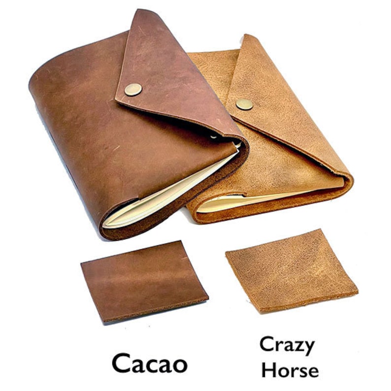 May include: Two leather-bound journals with a flap closure. The journal on the left is brown and the journal on the right is tan. Both journals have a metal button closure. The journals are labeled "Cacao" and "Crazy Horse".