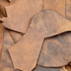 May include: A pile of brown leather offcuts with uneven edges. The leather has a distressed, worn appearance.