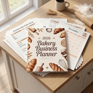 May include: A 2026 Bakery Business Planner with a watercolor design featuring croissants, rolling pins, and a whisk. Includes custom cake order forms and a calendar. The planner is open on a light-colored wooden surface.