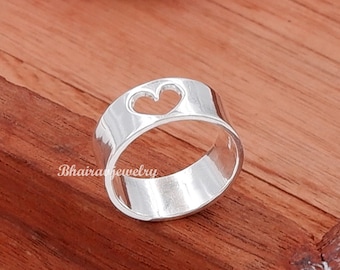 May include: A silver ring with a heart-shaped cutout. The ring is on a wooden surface.