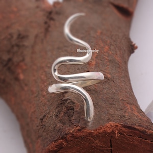 May include: A silver snake ring with a coiled design. The ring is made of sterling silver and is a unique and stylish piece of jewellery.