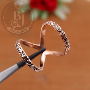 May include: A rose gold ring featuring an elaborate floral design. The ring is held by a tool, highlighting its detailed craftsmanship. The surface of the ring is decorated with delicate floral and leaf patterns, giving it an elegant and ornate look.