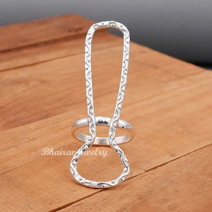 May include: A silver ring with a unique open design. The ring is made of a textured metal and has a delicate, intricate pattern.