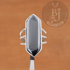 May include: A silver ring with a black gemstone in the shape of a long, pointed rectangle. The ring has a simple, modern design.