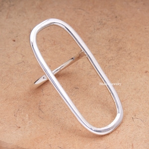 May include: A silver oval-shaped ring with a thick band. The ring is open on one side and has a simple, minimalist design.