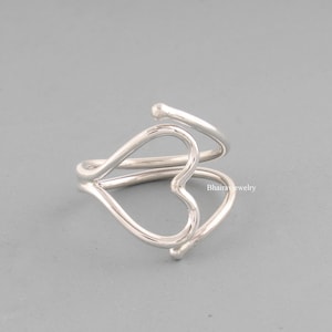 May include: A silver ring with a double heart design. The ring is made of a single piece of wire that is twisted to form the hearts.