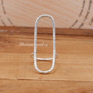 May include: A silver ring with a textured oval design. The ring is open on one side and has a smaller band on the other side.