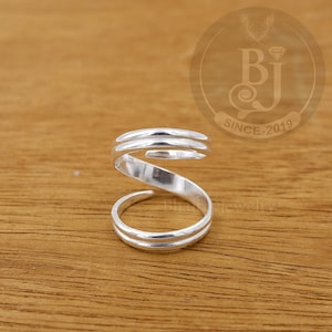 Könnte beinhalten: Silberner Spiralring mit strukturierter Oberfläche. Der Ring besteht aus zwei Bändern, die sich ineinander verdrehen.