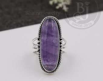 Può includere: Un anello d'argento con una grande ametista ovale. L'anello ha un design dettagliato con una fascia intrecciata e piccole perle.