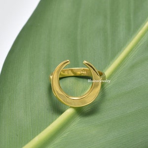 Può includere: Un anello a forma di mezzaluna dorata con una superficie liscia e arrotondata. L'anello è in argento sterling 925 e ha un design minimalista.