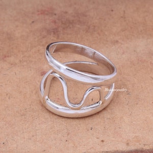 Puede incluir: Anillo de plata con un diseño abierto único que presenta un patrón de línea ondulada. El anillo está hecho de dos bandas, una de las cuales es una banda simple y la otra tiene el diseño abierto.