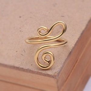 May include: A gold-coloured ring with a unique, abstract design. The ring is made of a single piece of wire that is twisted and shaped into a swirling pattern.