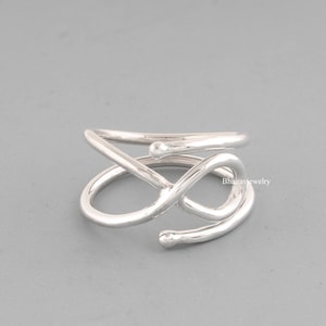 May include: Silver ring with a twisted, infinity-like design. The ring is made of a single piece of metal that is bent and twisted to create the design.