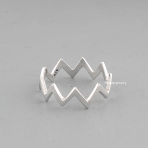 Può includere: Un anello d'argento con un design a zig-zag. L'anello è contrassegnato con il numero "925" all'interno.