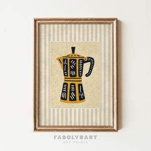 May include: Framed art print featuring a yellow and black coffee maker illustration. The artwork is set against a beige background with a striped pattern and is enclosed in a gold-colored frame. The print includes the text "FABOLYNART ART PRINTS".
