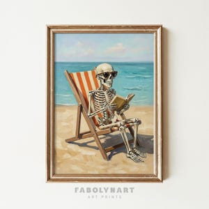 May include: A framed art print depicts a skeleton wearing sunglasses, relaxing in a beach chair, and reading a book. The skeleton is on a sandy beach with the ocean and sky in the background. The chair has red and white stripes.