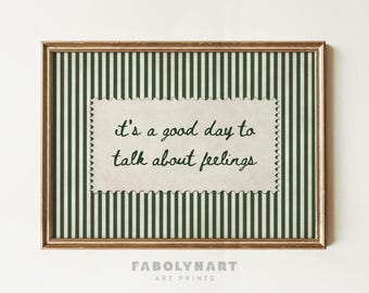 May include: A rectangular wall art print in a metallic frame featuring a dark green and white vertical striped background. Centered is a cream-colored, postage stamp-shaped paper cutout with the black text: it's a good day to talk about feelings.