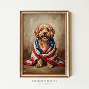 May include: A framed art print featuring a smiling, light brown dog wrapped in an American flag. The dog is the focal point, with the flag's red and white stripes and blue star field prominently displayed. The artwork has a vintage, painterly style.
