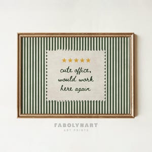 May include: A framed wall art print featuring a dark green and white vertical striped background. In the center, a cream-colored postage stamp shape displays five yellow stars above the text: cute office, would work here again.