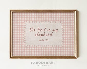 Puede incluir: Una lámina decorativa rectangular en un marco dorado con un fondo de patrón de cuadros vichy en rosa claro y blanco. Centrada hay una etiqueta festoneada de color crema con el texto en marrón: the lord is my shepherd, psalm 23. Diseño sencillo.