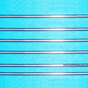 Op de afbeelding: Zes zilverkleurige breinaalden zijn horizontaal gerangschikt tegen een helderblauwe achtergrond. Elke naald heeft aan beide uiteinden een langwerpig oog. De naalden zijn recht en lijken van metaal te zijn.