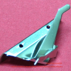 May include: A silver-colored metal part with a curved handle and two small holes. The part has a triangular shape with a curved edge and is set against a pink background. The text "CREATIVECOUNTER" is visible.