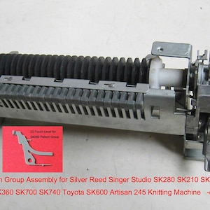 May include: A silver Pattern Group Assembly for Silver Reed Singer Studio knitting machines. It has a black ribbed section, a white cylinder, and a red and blue square. A red card displays text: "(2) Tooth Lever for SK240 Pattern Group".