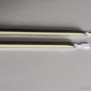 Peut inclure: Deux objets longs, fins, blancs et noirs avec une bande jaune clair. Les objets ont une forme rectangulaire avec une extrémité blanche crantée. Les objets sont placés parallèlement l'un à l'autre sur une surface gris clair.