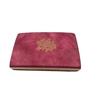 May include: A rectangular, burgundy-colored box with a gold floral design on the top. The box has a gold trim around the edges. The surface of the box has a velvet-like texture.