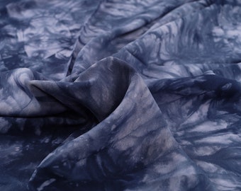 Puede incluir: Primer plano de una tela fluida con un estampado tie-dye en tonos azules y blancos. La tela parece suave y ligera, con pliegues y arrugas visibles. El patrón de tinte crea un efecto marmoleado.