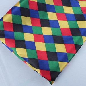 May include: A colorful, diamond-patterned fabric in red, yellow, green, blue, and black. The fabric is folded, showing the pattern at an angle. The material appears to be a smooth, possibly satin, textile.