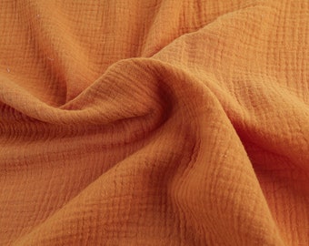 Puede incluir: Primer plano de una tela suave y texturizada de color naranja cálido. La tela está arrugada y doblada, mostrando su textura arrugada.