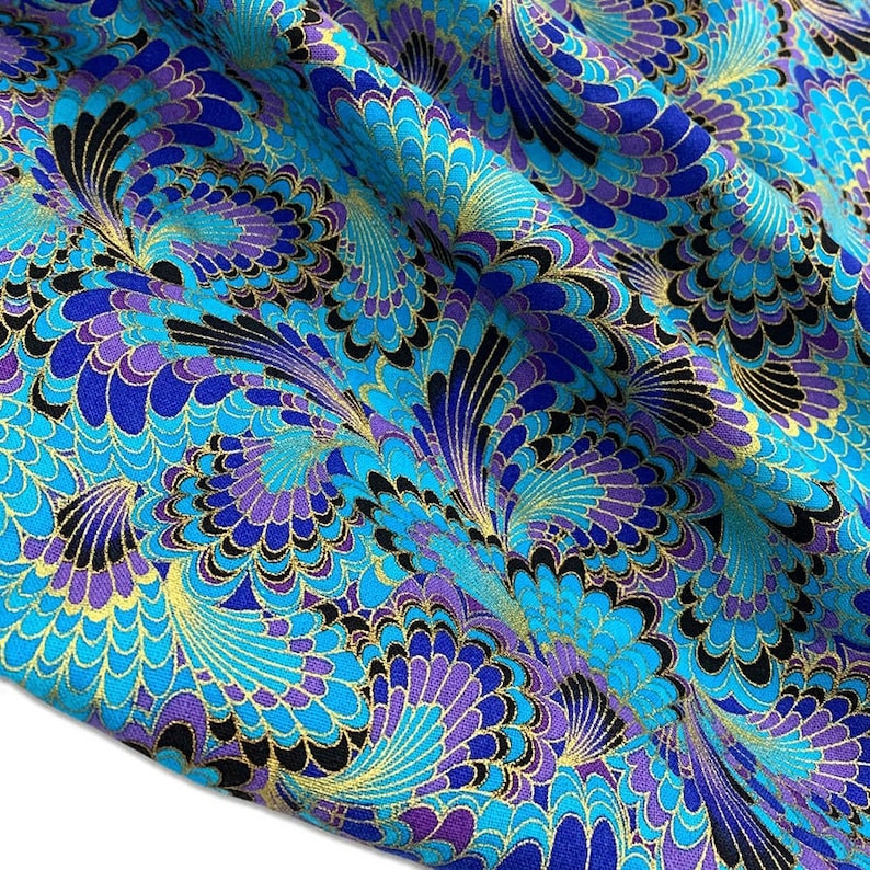 K&ouml;nnte beinhalten: Blauer und lilafarbener Stoff mit einem sich wiederholenden Muster aus stilisierten Pfauenfedern. Der Stoff hat einen goldenen Metallic-Glanz.