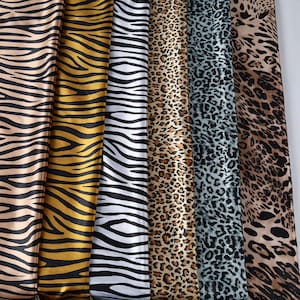 Può includere: Assortimento di tessuti con stampe animalier, tra cui motivi zebrati e leopardati. I tessuti presentano una varietà di colori, tra cui nero, bianco, oro e marrone. I tessuti sono disposti verticalmente, mostrando i diversi disegni.