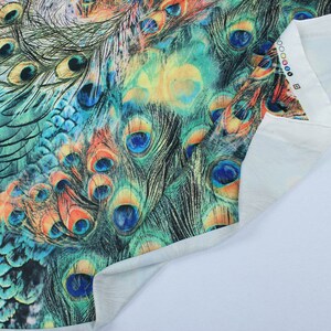 May include: Close-up of a fabric with a peacock feather print. The fabric is a light blue color with a white background. The peacock feathers are a vibrant green, blue, and orange.