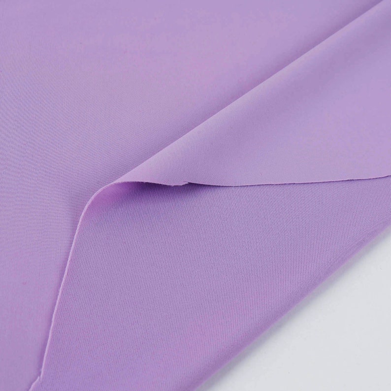 May include: A close-up of a soft, lilac-colored fabric. The fabric is folded in half, showing the texture of the material.
