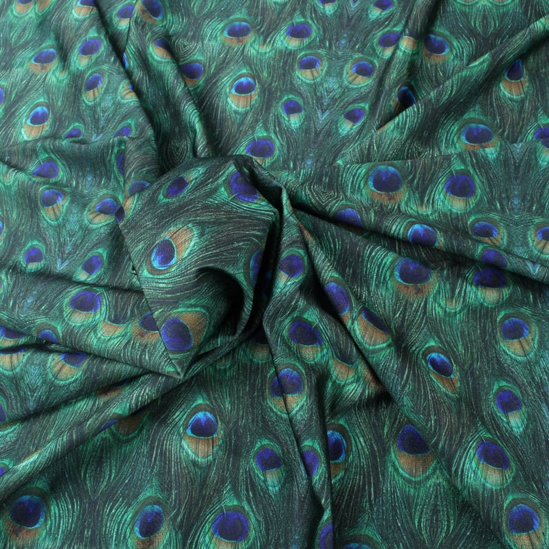 May include: Green fabric with a peacock feather pattern. The fabric is folded and shows the texture of the material.
