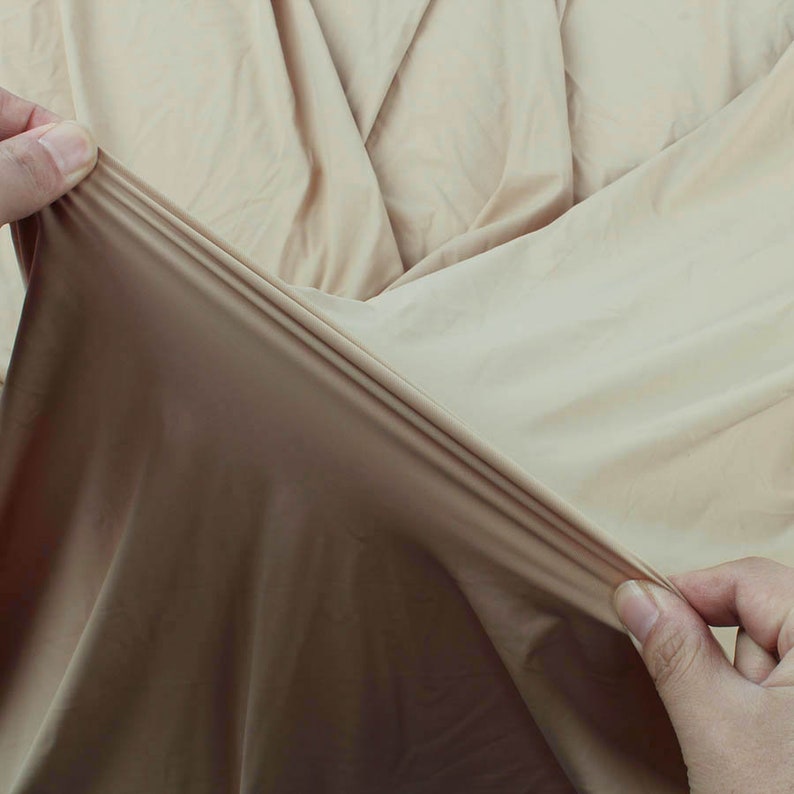 May include: Close-up of a light brown fabric being stretched and pulled. The fabric is smooth and has a slight sheen.