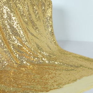 May include: Gold sequin fabric with a shiny, iridescent finish. The fabric is draped and folded, showcasing its texture and drape.