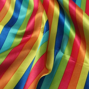 May include: A close-up of a vibrant fabric with bold, diagonal stripes in a rainbow of colors. The stripes include red, orange, yellow, green, blue, and purple. The fabric has a shiny, satin-like texture, with soft folds and curves.