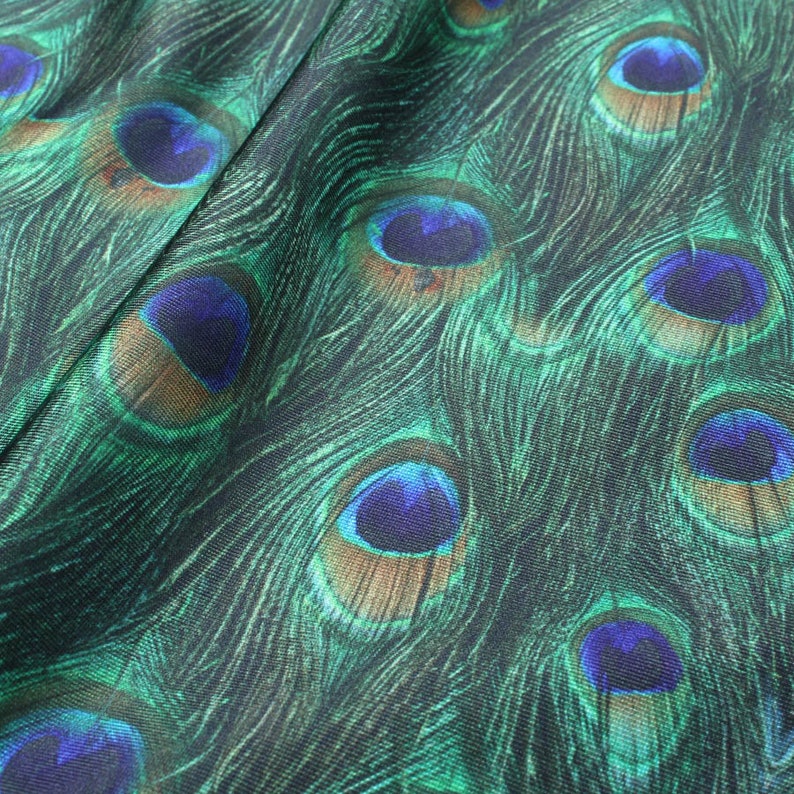 May include: Close-up of a fabric with a peacock feather pattern. The fabric is green and blue with brown accents. The feathers are arranged in a repeating pattern.