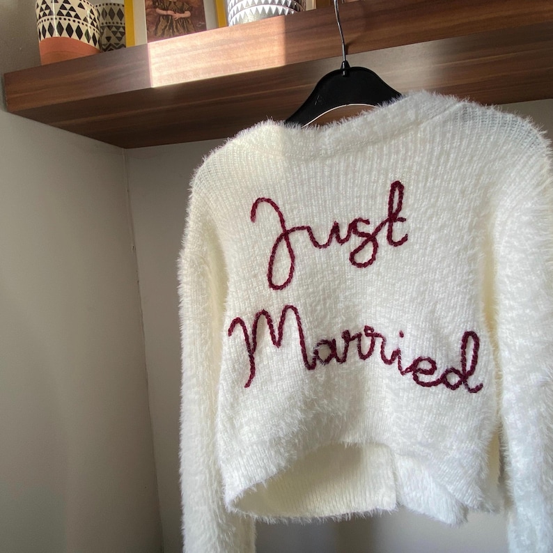 May include: White fuzzy sweater with the words "Just Married" embroidered in burgundy.